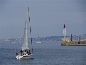 Sailing boat on the open sea, in the background more boats and a lighthouse, Marseille on the