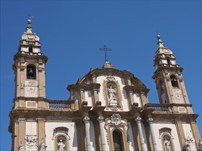 Facade of a historic church with two towers and a cross against a blue sky, palermo in sicily with