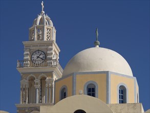 A church tower with a clock and a domed church with a cross against a clear blue sky, The volcanic
