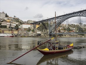 Picturesque wooden boat on a river in front of a bridge and a hill town in Portugal, Colourful