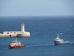 Two boats sailing on the blue sea near a lighthouse under a clear sky, Valetta, Malta, Europe
