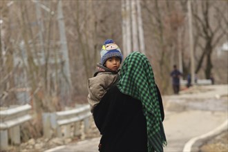 A mother carrying her child on a rural road during winter