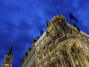 Illuminated building with ornate details and flags against a deep blue sky at night, blue hour in a