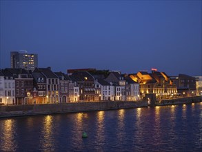 Illuminated row of houses on the riverbank in the evening, Maastricht, Netherlands