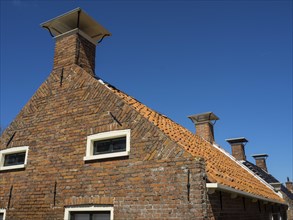 House with several chimneys and orange-coloured roof tiles under a clear blue sky, Enkhuizen,