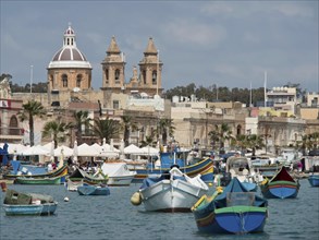 Colourful boats in the harbour in front of historic buildings and church with calm water under a