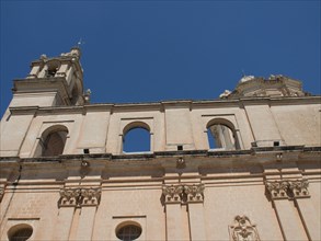 Monumental church facade with columns and decorative details under a clear sky, the town of mdina