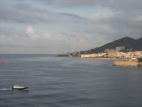 A small boat on a calm sea with a view of a coastal town and hills, Corsica, ajaccio, France,