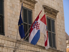Three flags, including the European and Croatian flags, fly in front of a historic building with