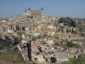 Panoramic view of a historic city on a hill dominated by a large castle under a clear blue sky,