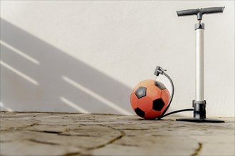 Hand pump inflating a red soccer ball with a white background