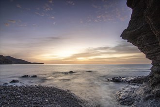 Sunrise with sea view in a lonely bay. rocky coast in warm colours. Landscape with a lava stone