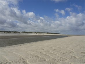 A wide, empty beach under a cloudy sky, with dunes in the background, Spiekeroog, Germany, Europe