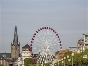 City view with a red Ferris wheel, church tower and historical buildings under a cloudy sky, Ferris