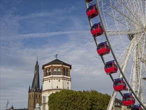 Church tower and historic building next to a Ferris wheel with red gondolas under a cloudy sky,