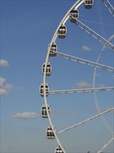 Partial view of a Ferris wheel with several cabins in front of a clear blue sky, the beach of