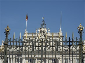 A historic fence with lace and ornate decorations in front of a building with a flag under a blue