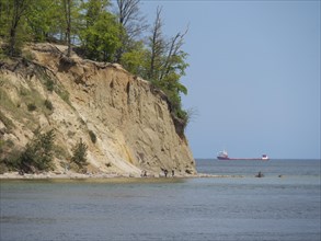 A boat near a rocky coast with trees and blue sky in the background, spring on the Baltic Sea beach
