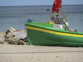 A green fishing boat with a red flag lies on the beach near rocks, green and yellow fishing boats