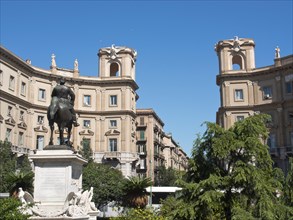 A statue on a pedestal in an urban square surrounded by classical buildings and green spaces under