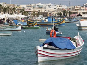 Colourful fishing boats are moored in the harbour with city buildings in the background, many