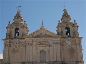 Front view of a historic church with two bell towers and clocks, the town of mdina on the island of