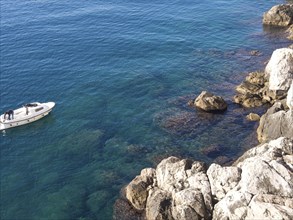 Boat near rocky coast in clear, blue water with rock formations in the sea, the old town of