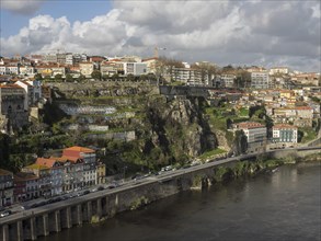 View of a city on a river, lined with buildings on a rocky cliff under a cloudy sky, spring in the