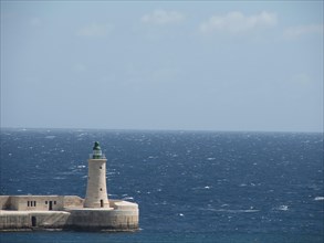 A lighthouse on a pier by the ocean, under a clear blue sky, Valetta, Malta, Europe