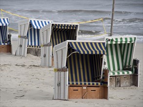 Several empty beach chairs with striped awnings stand on the beach near the sea, a volleyball net