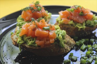 Bruschetta with fresh salmon, avocado, dill, and green onions on a plate
