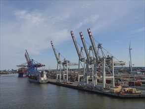 A view of an industrial harbour with several cranes, containers and a cargo ship at the quay, large