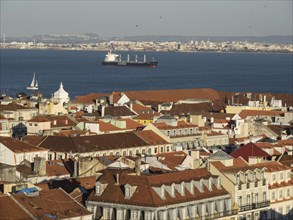 Wide angle view of a historic city with red roofs and a cargo ship in the background in the water,