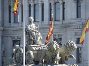 Historic fountain with a statue and two lions flanked by Spanish flags, Madrid, Spain, Europe