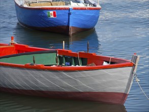 Red and grey fishing boat in the water, slender shapes and calm water surface, The city of Bari on