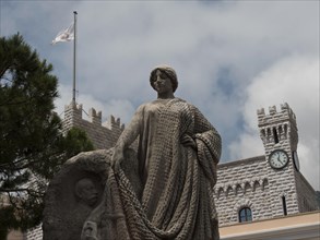 Statue in front of a castle with clock tower and flag, surrounded by clouds, Monte Carlo, Monaco,