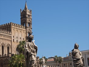 Gothic cathedral and sculptures under a clear blue sky, surrounded by palm trees and historic