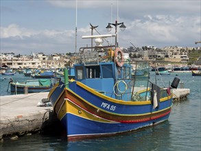 Colourful fishing boat at the harbour, surrounded by calm water and city scenery in the background,