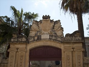 Majestic archway adorned with a coat of arms, surrounded by lush palm trees under a clear sky, the