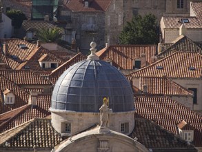 Large church cupola with a statue, surrounded by the red roofs of a historic city, the old town of