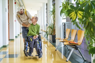 Disabled man with wheelchair and friend walking along in the university corridor