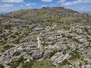 A rocky and dry landscape with two buildings under a cloudy sky, aerial view, karst mountains,