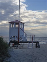 White and red beach tower on wheels on a sandy beach under a cloudy sky with the sea in the