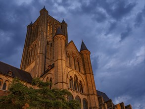 Large gothic style church tower, illuminated at dusk with cloudy sky, blue hour in a medieval town