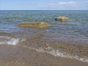 Clear sea water gently meets stones on the beach under a sunny, blue sky, spring on the Baltic Sea