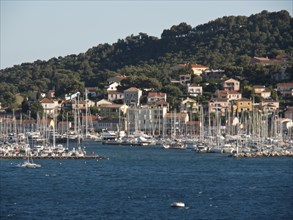 A coastal town with many sailing boats and yachts in the harbour in front of wooded hills, la seyne