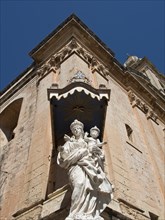 A statue of the holy mother and child in front of the corner of a historic building, the town of