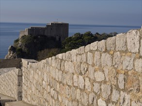 Historic fortress on a rocky cliff, surrounded by a massive stone wall, overlooking the blue sea on