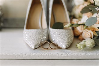 Glittery high heels with wedding rings in front, surrounded by delicate flowers in a romantic