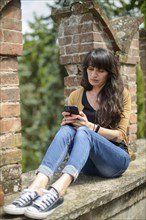 Young woman in casual clothing focused on conversation with smartphone in a peaceful garden with